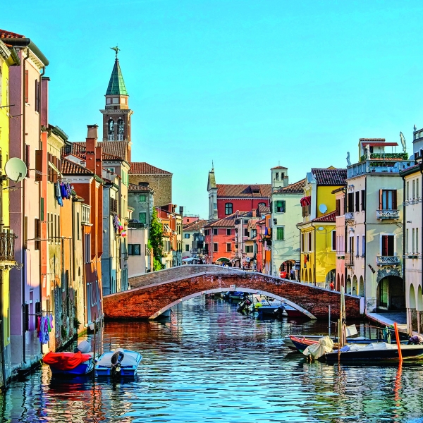 Bright multicolored buildings line both sides of a urban canal that is connected by pedestrian arch bridges.