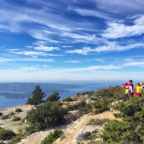 Tourists take photos from the vantage of a look off point, revealing the ocean and a distant mountain range.