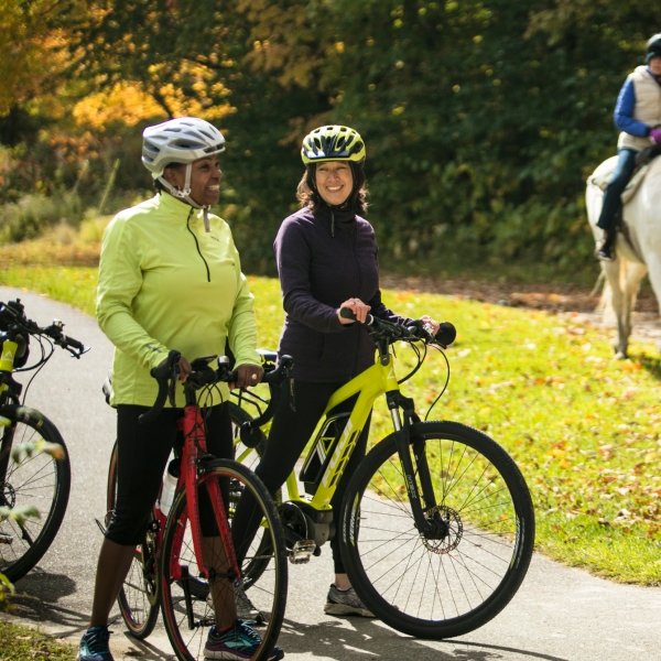Two bikers on a bike tour in Stowe, Vermont. On bike path with people riding horses passing by